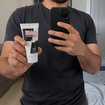 A customer holding the 30 ml Rhino Long Power Cream tube up to a mirror