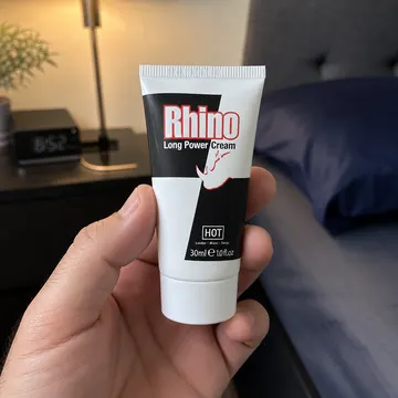 The 30 ml Rhino Long Power Cream tube held in one hand beside a bedside table